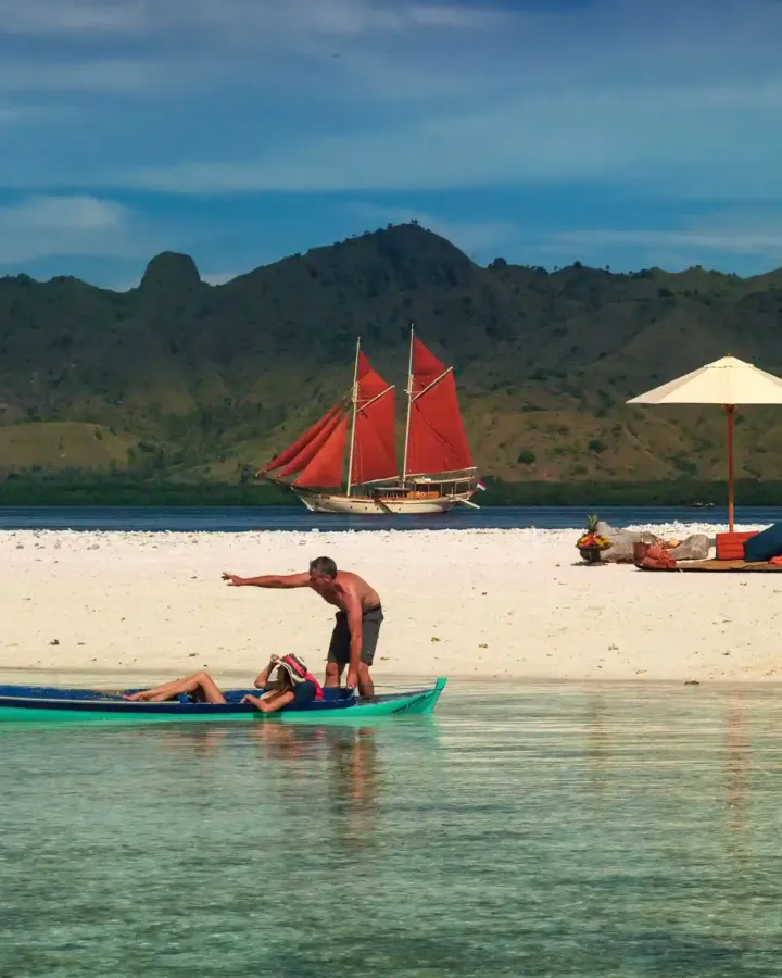 Red-sailed phinisi seen from a beach in Komodo